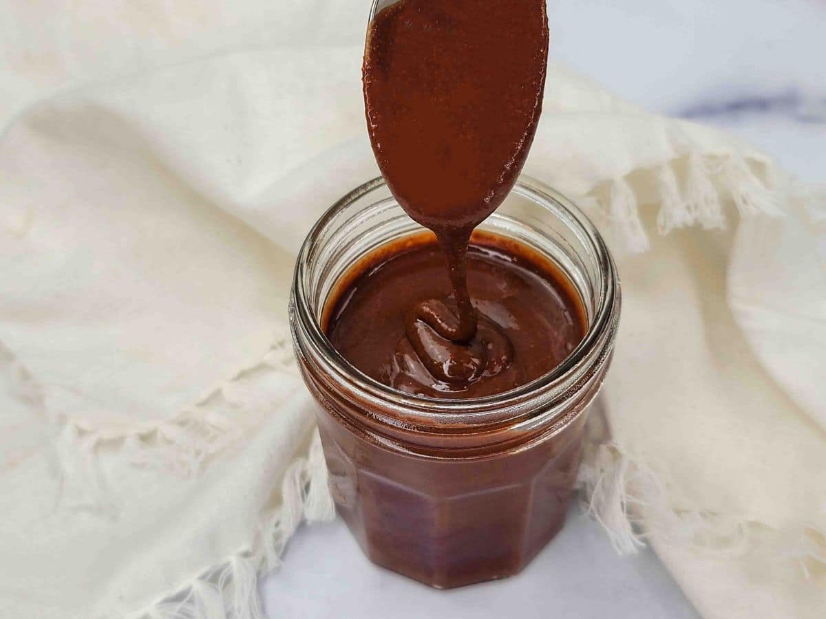A spoon pouring vegan hazelnut spread into a jar.