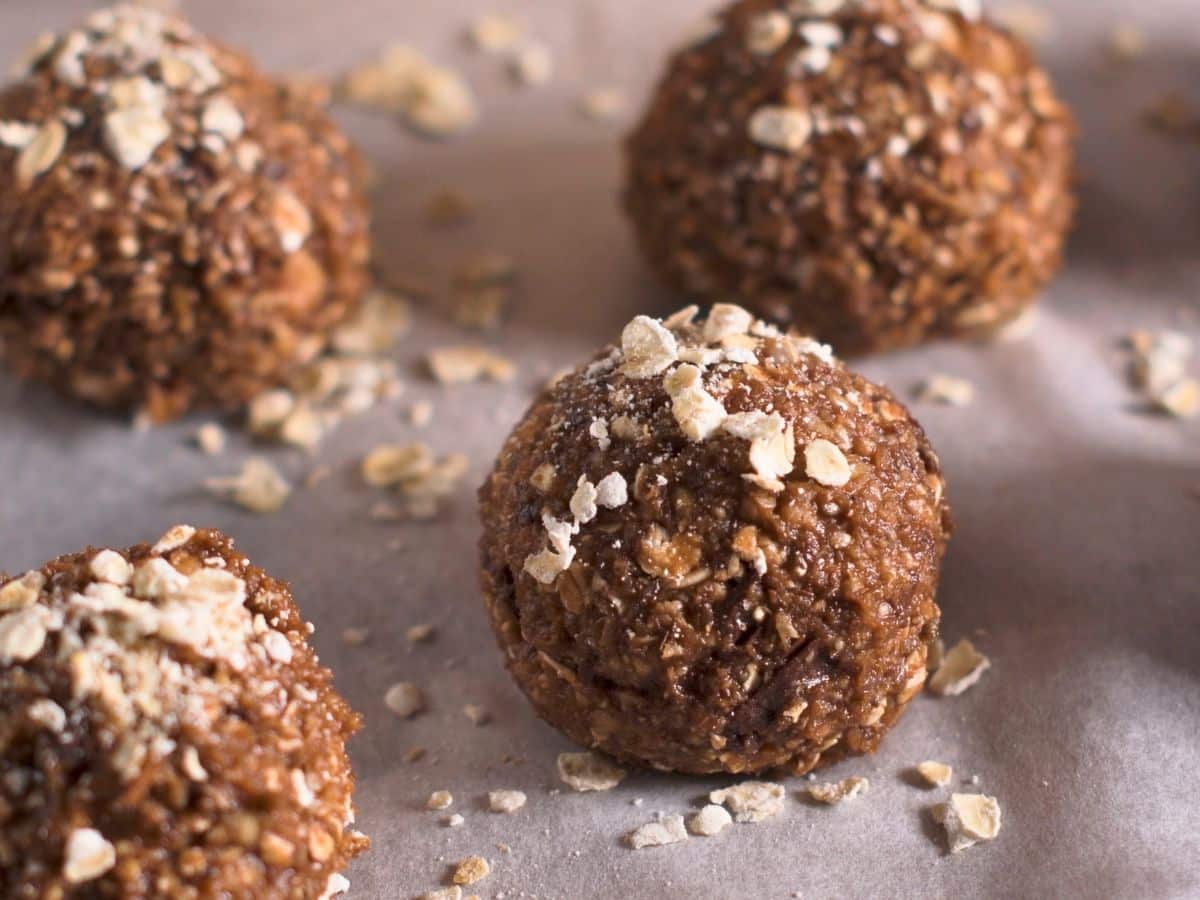 Close-up of several oatmeal energy balls covered with scattered oats, placed on a parchment paper.