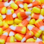 Close-up of candy corn with hues of orange, yellow, and white. Text reads "Candy Corn" and "Best Vegan Options" with "Sage AlphaGal" logo below.