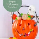 A plastic pumpkin container filled with assorted vegan candies, including lollipops and chocolates, with a small ghost decoration on top. Text overlay reads "30+ Vegan Halloween Candies.