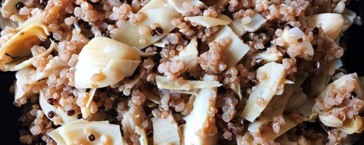 Close-up of a quinoa salad mixed with sliced artichoke hearts.