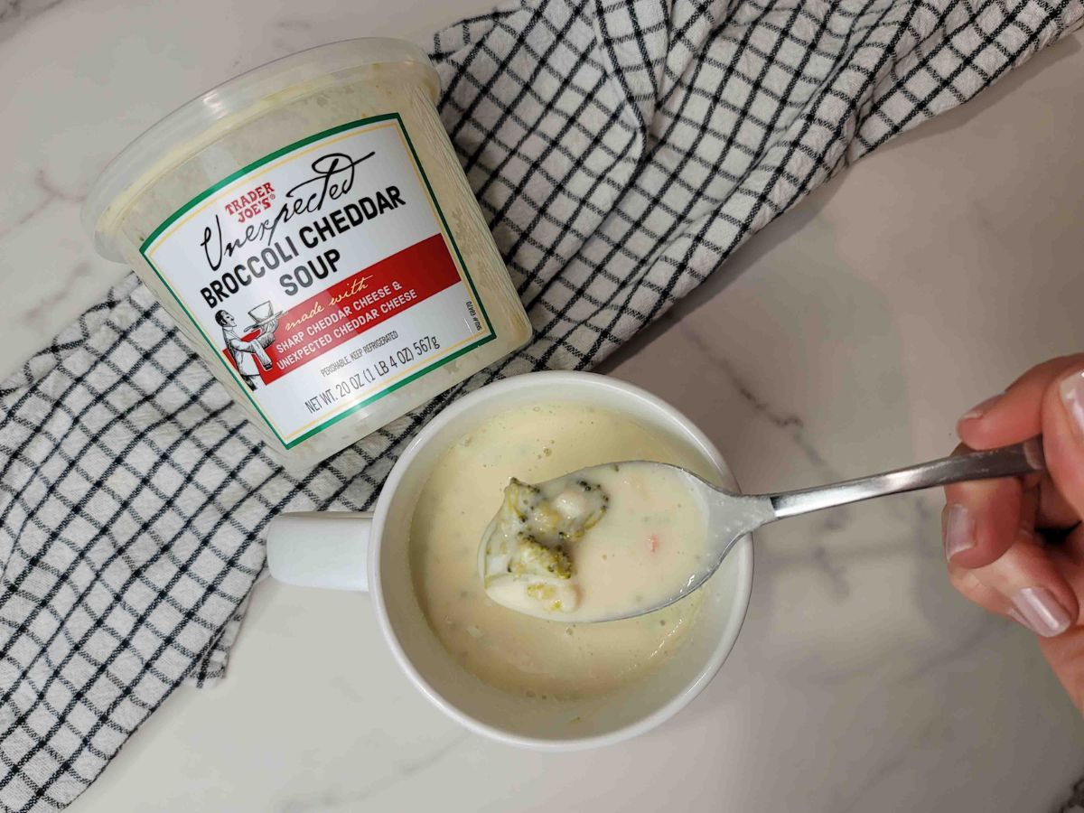 A person holding a spoon next to a cup of Trader Joe's soup.