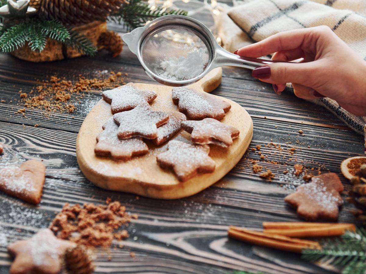 A person is pouring sugar on cookies on a wooden table.