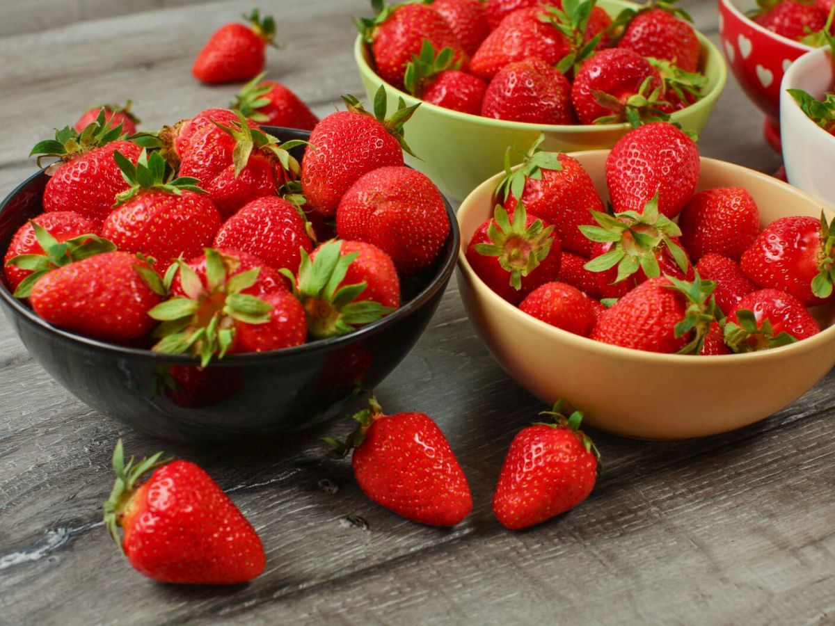 Several bowls of fresh strawberries sitting on a kitchen table.