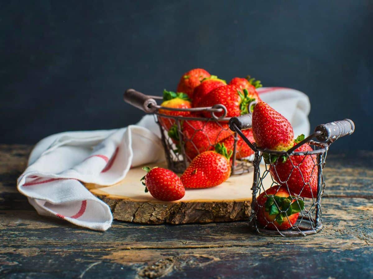 Organic fresh strawberries in a wire basket on a dark wood table.