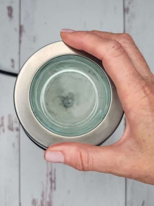 A hand holds a glass cup of water viewed from above on a wooden surface.