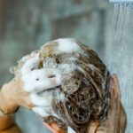 A person washing their hair under a shower with lots of foam, with the text "What is Vegan Shampoo?" at the top.