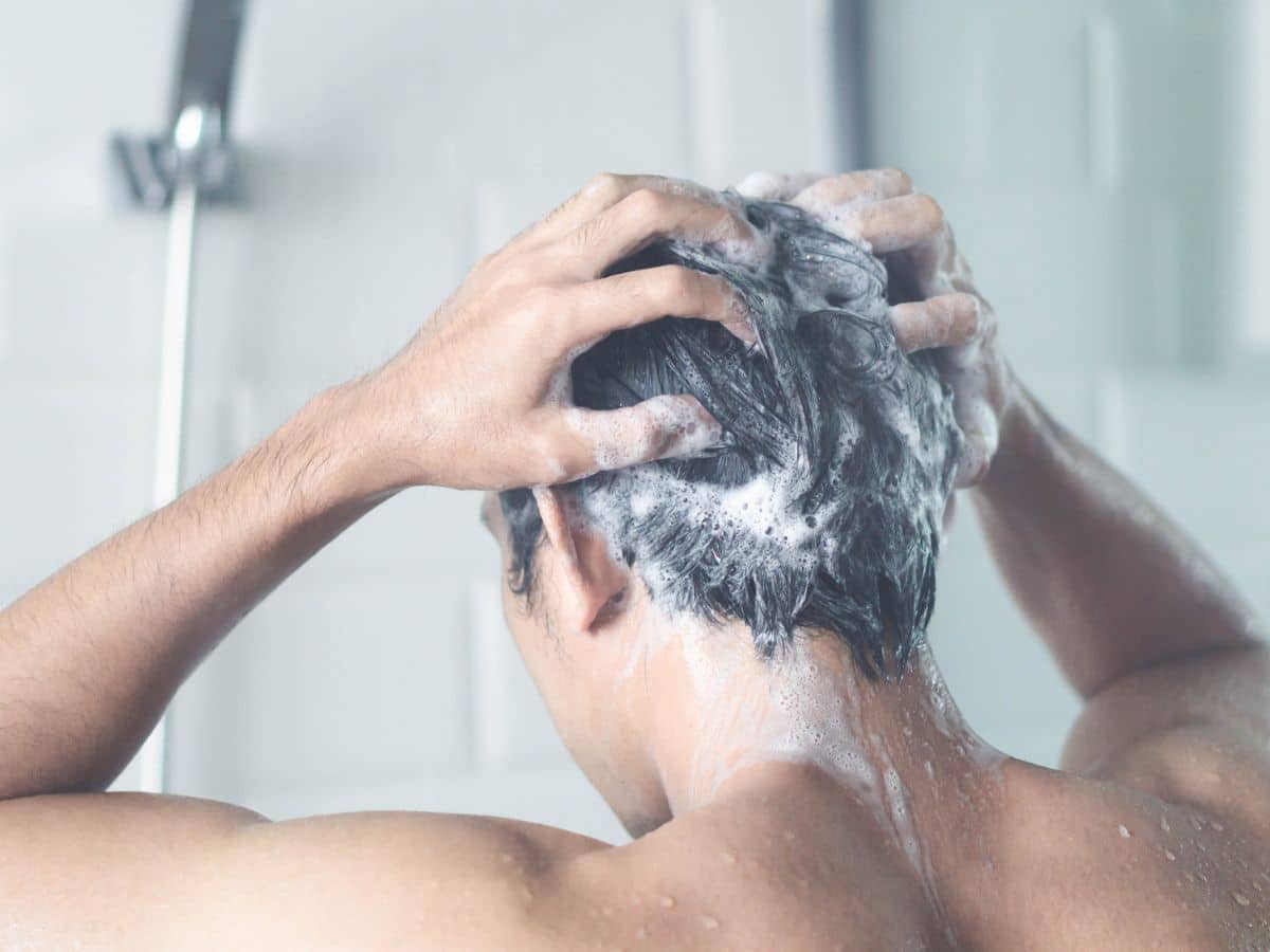 Person washing hair with shampoo in a shower. The person's hands are massaging the shampoo into a lather.