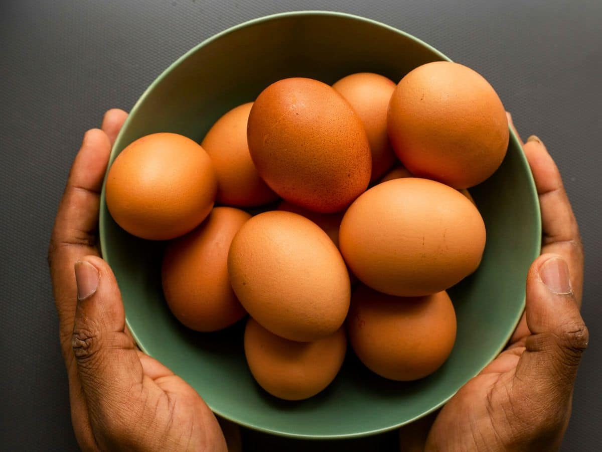 Two hands holding a green bowl filled with several brown eggs.