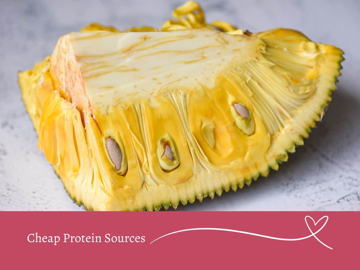 A close-up of a partially sliced jackfruit showing its yellow flesh and seeds. Below is a banner that reads "Cheap Protein Sources" with a heart symbol.