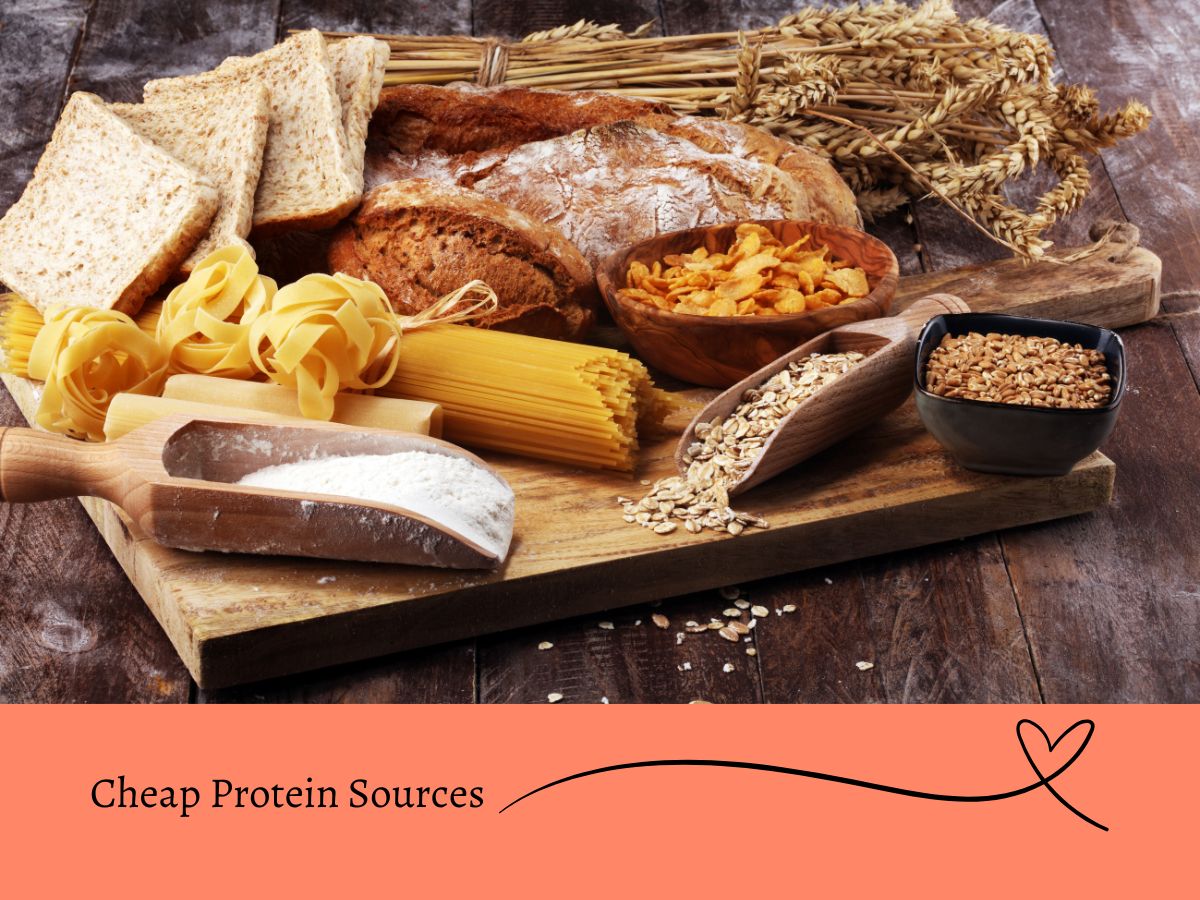 A wooden table holds an assortment of bread, pasta, grains, and flour, with wheat stalks in the background. A banner below reads "Cheap Protein Sources.