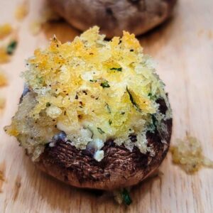 A stuffed mushroom cap topped with golden breadcrumbs and herbs on a wooden surface.