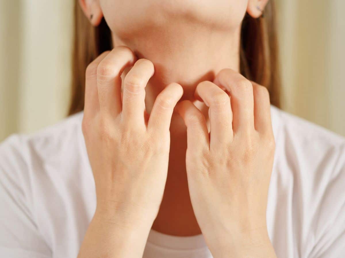 Person scratching their neck with both hands, wearing a white shirt.