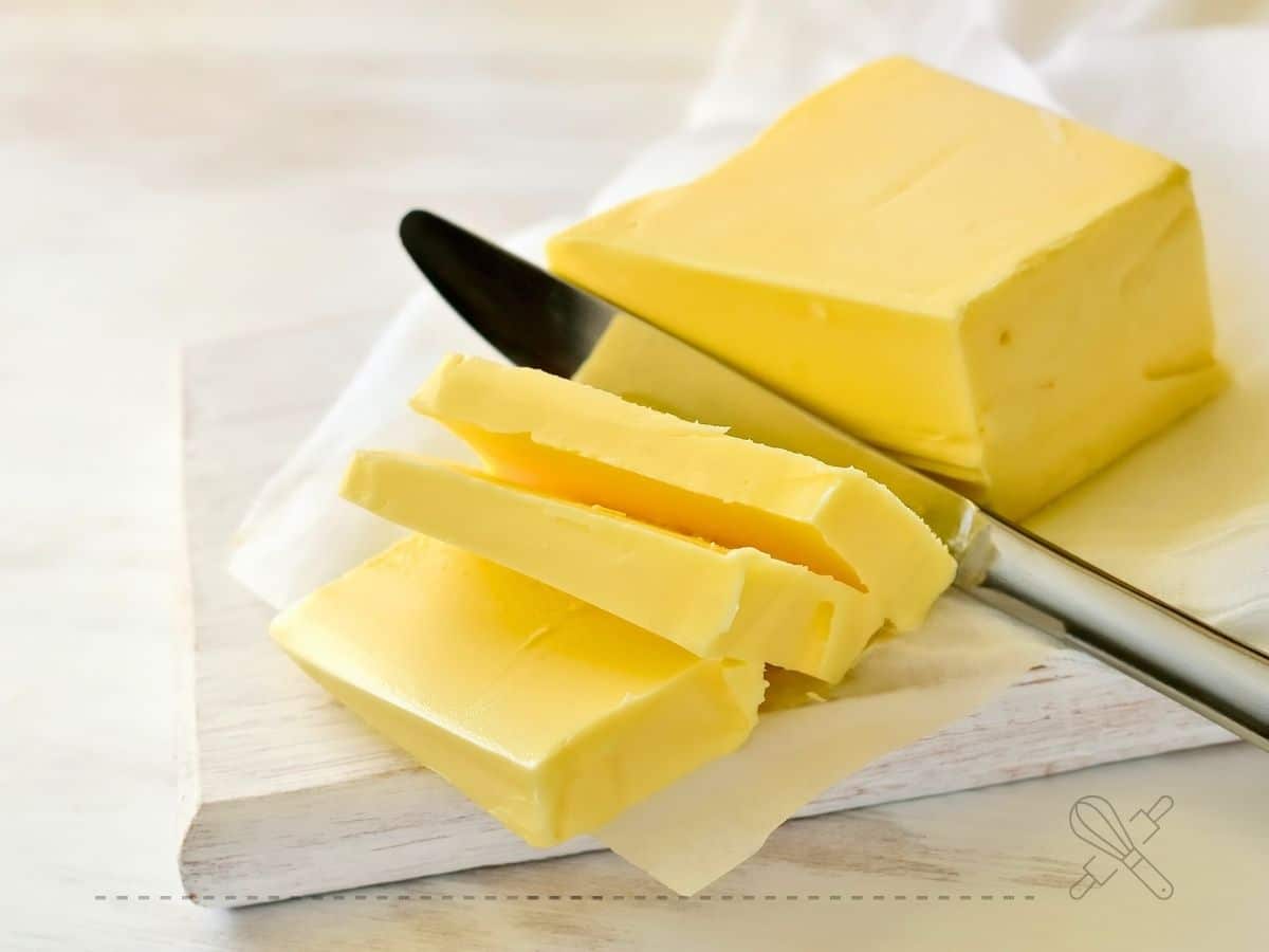 Sliced butter on a wooden board with a knife beside it.