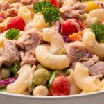 A bowl of macaroni salad with canned tuna, cherry tomatoes, green olives, red onions, and parsley. Text reads "Easy Canned Tuna Meals for Lunch or Dinner.
