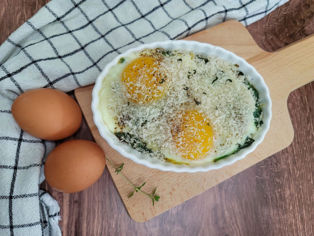 A gratin dish of baked eggs florentine on a wooden table.