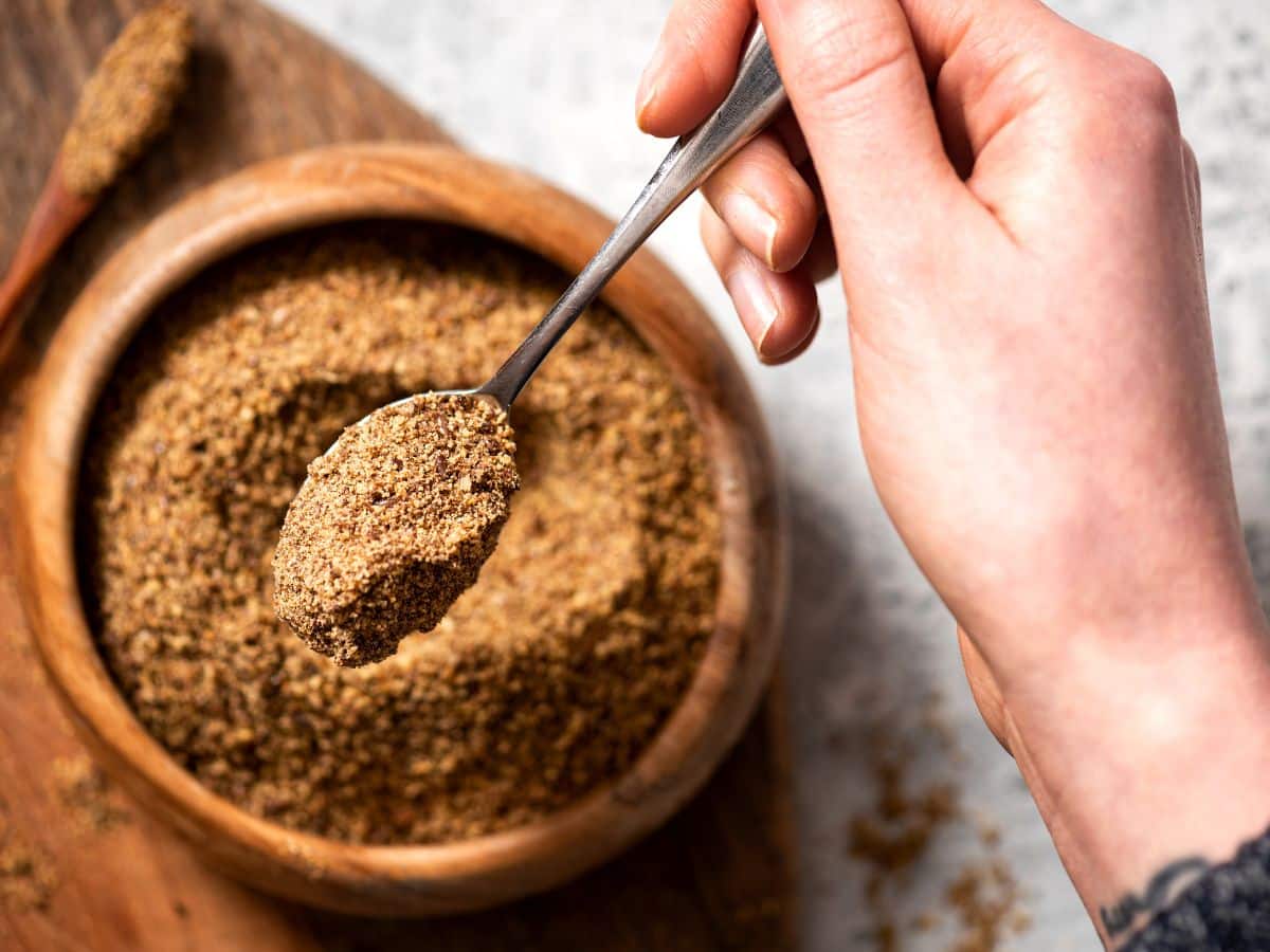 A woman holding up a spoon of ground flaxseed