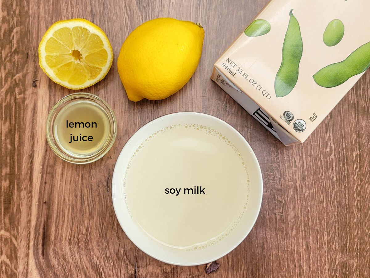 Wooden table with lemon juice and soy milk needed to make vegan buttermilk recipe.