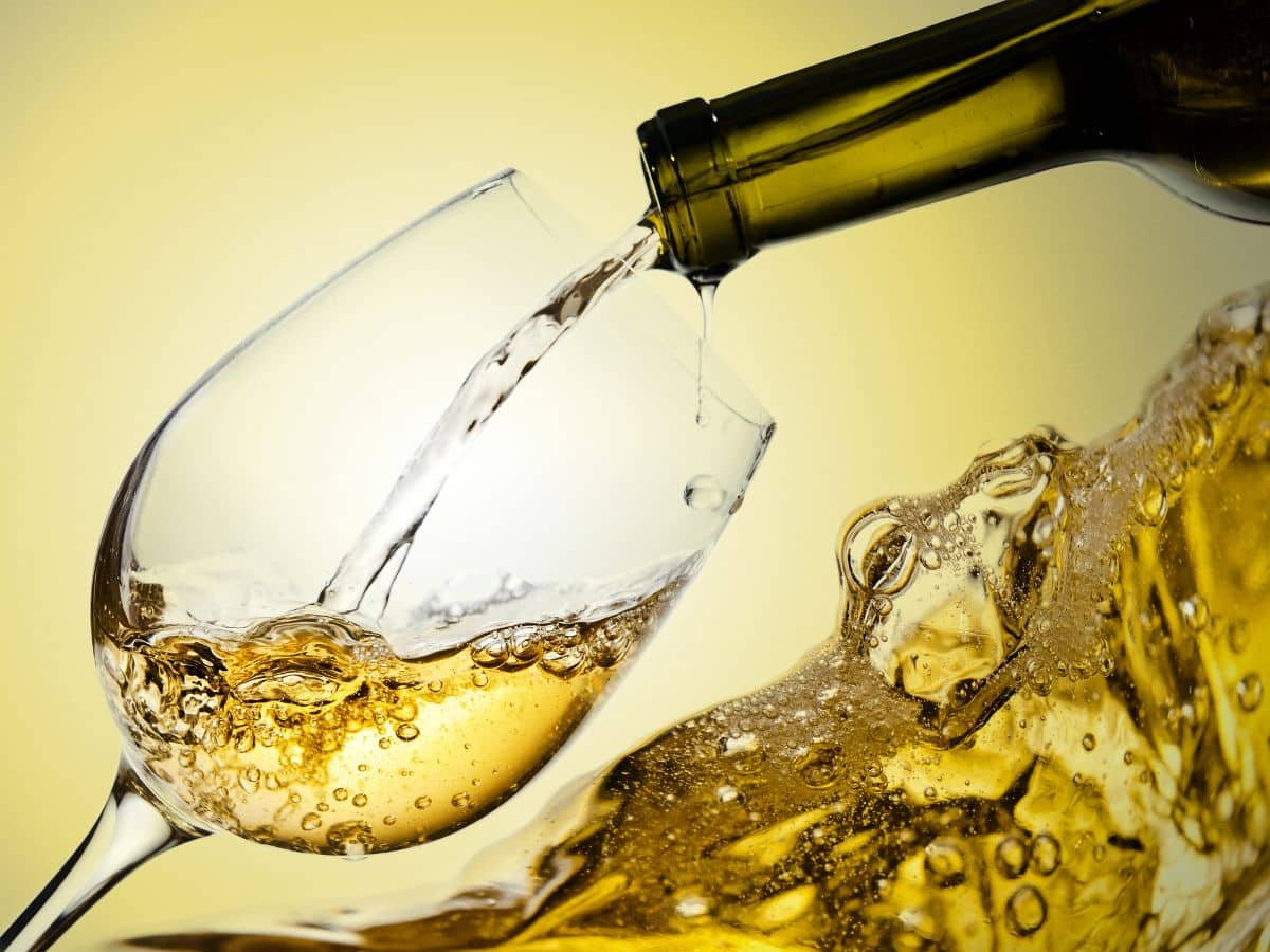Green bottle pouring white wine into a wine glass.