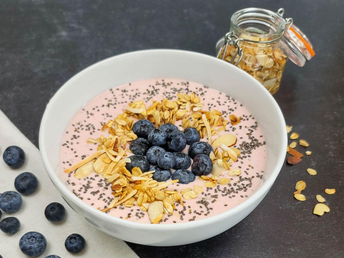A bowl of strawberry Greek yogurt topped with blueberries, chia seeds, and granola.
