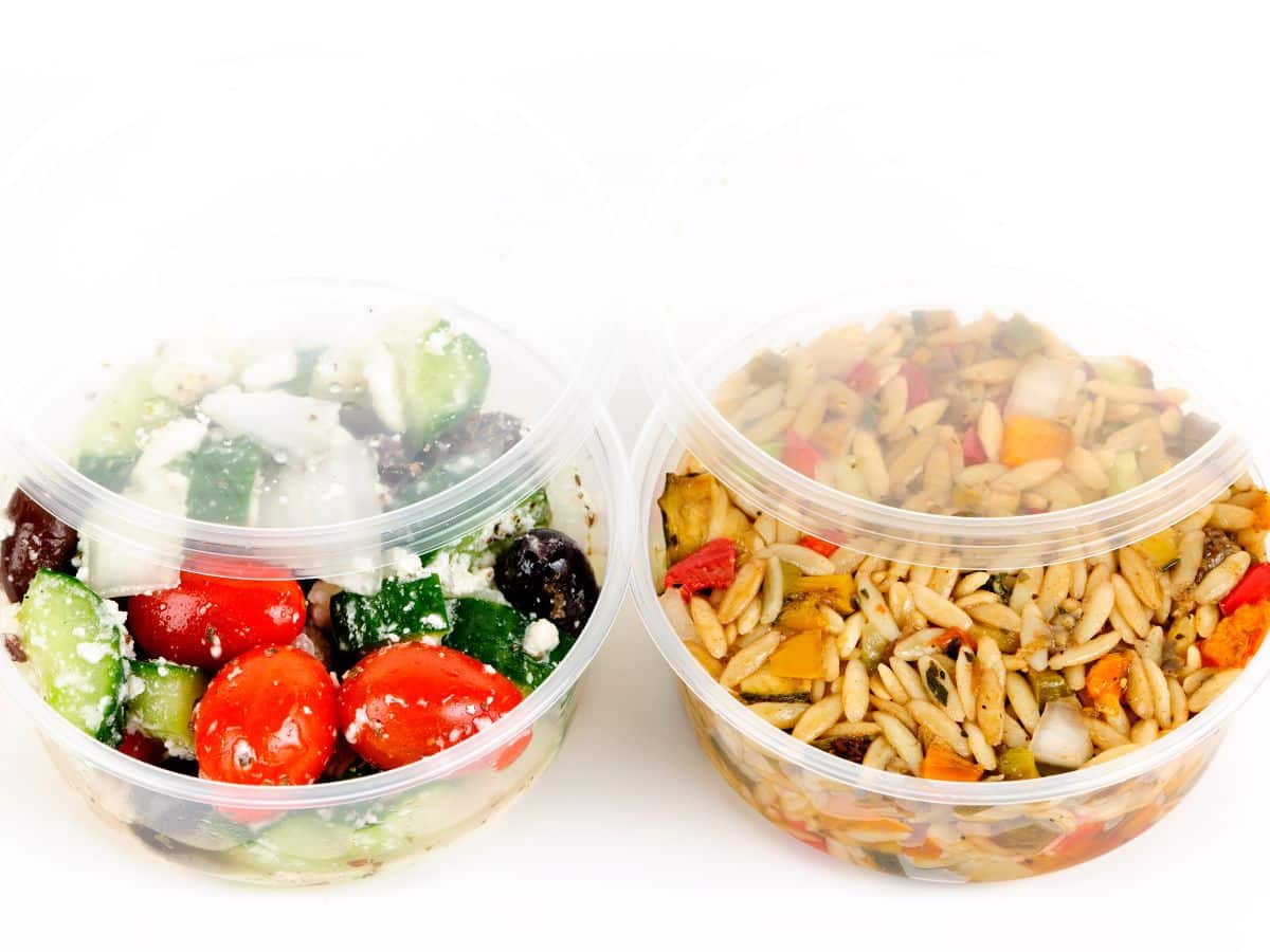 Two plastic deli containers with salad and vegetables in them.