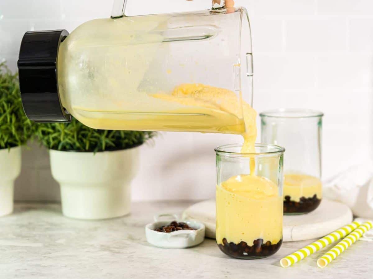 A person pouring a mango smoothie into a glass.
