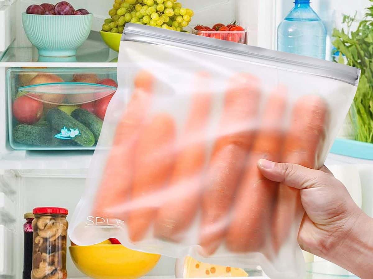 A person holding a bag of carrots in a reusable food storage bag in front of an open refrigerator.