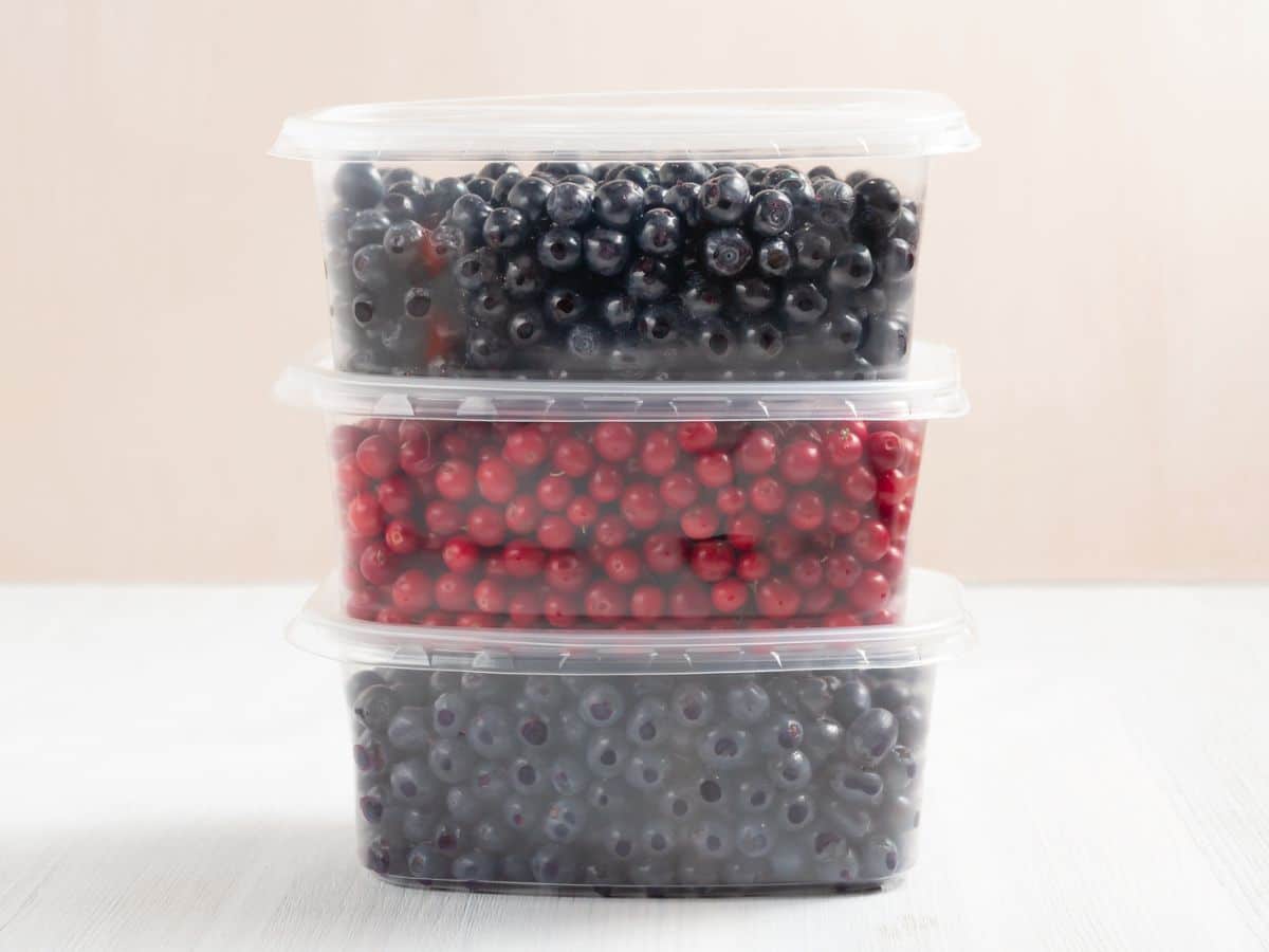 Three plastic food containers filled with berries on a wooden table.