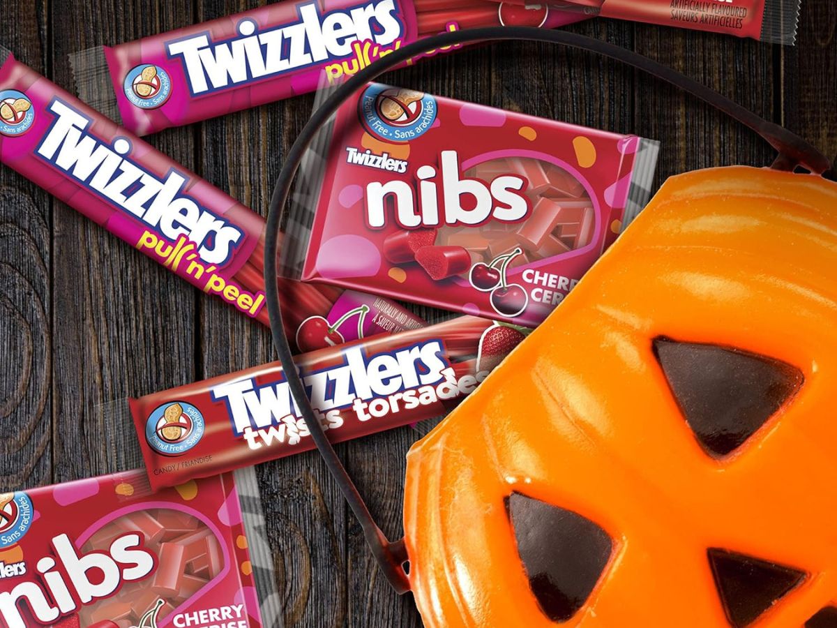 An assortment of Twizzlers Halloween candy by a plastic pumpkin trick-or-treat bucket.