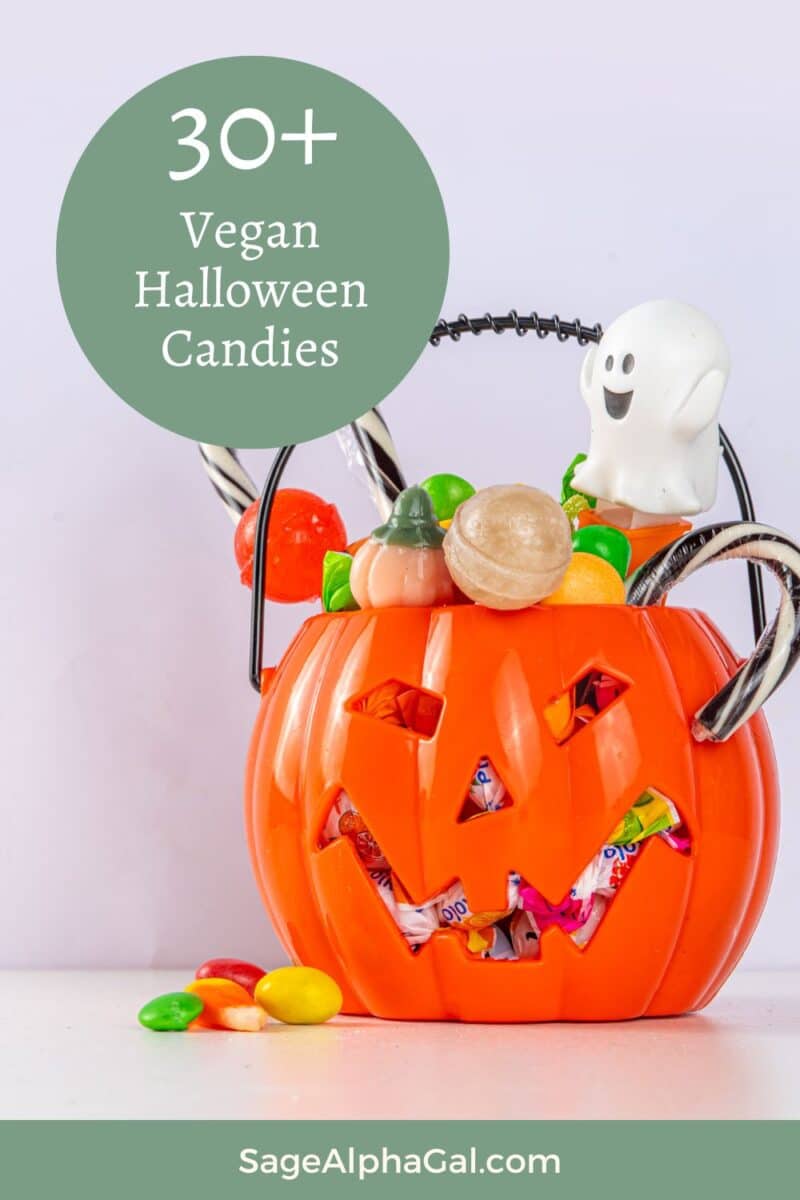 A plastic pumpkin container filled with assorted vegan candies, including lollipops and chocolates, with a small ghost decoration on top. Text overlay reads "30+ Vegan Halloween Candies.