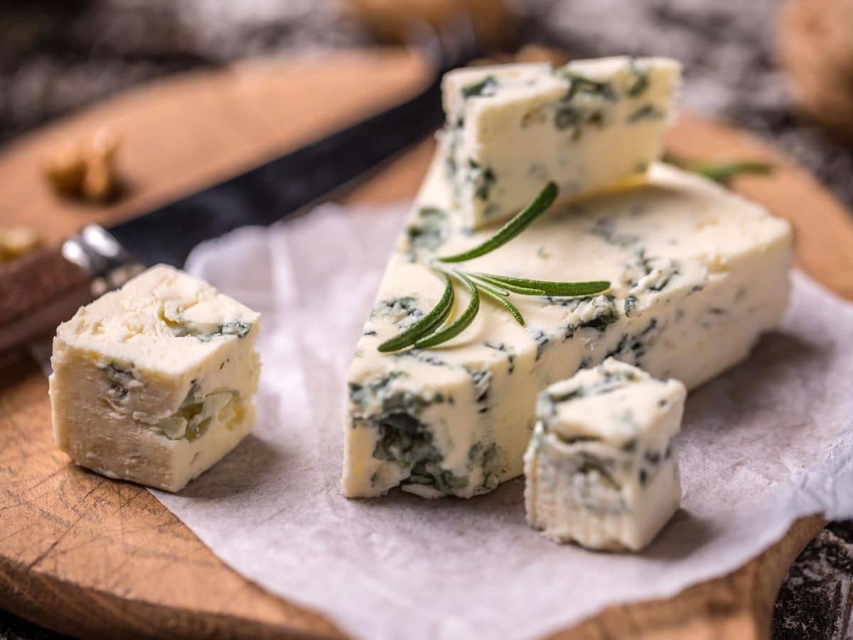 French Roquefort cheese with sprigs of rosemary on a wooden cutting board.