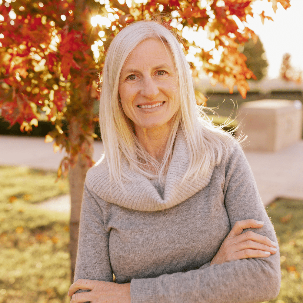 Sage Scott in a gray sweater standing in front of a tree in the fall.