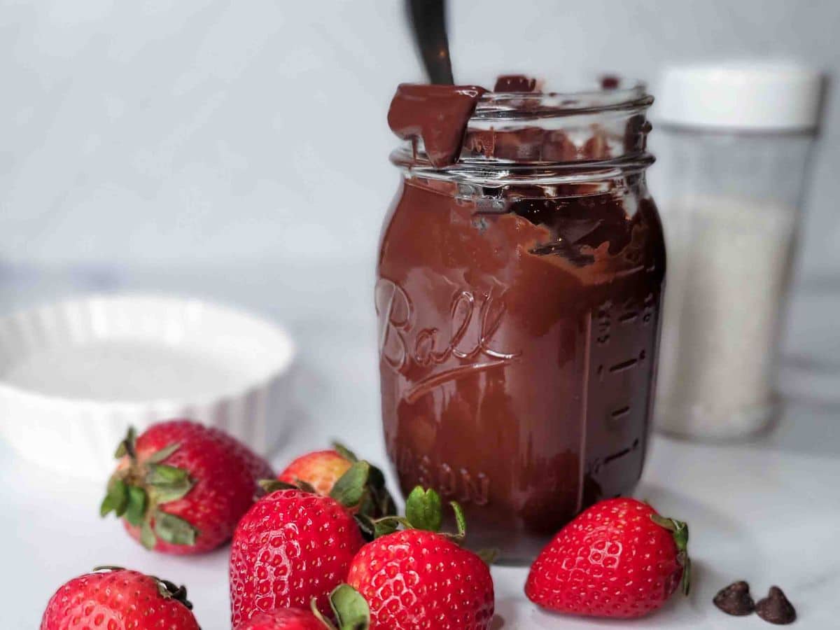 Fresh strawberries ready to be dipped in a jar of melted chocolate.