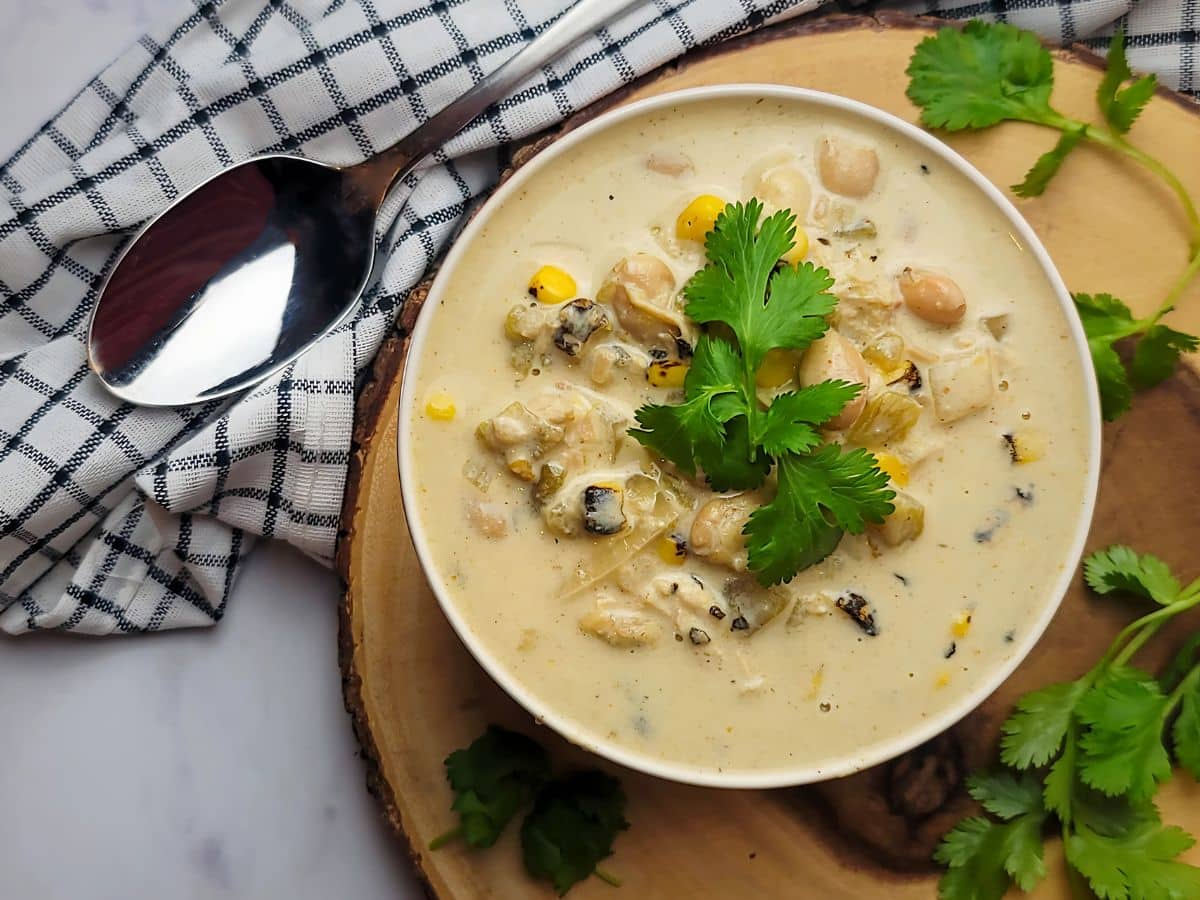 A bowl of creamy white chicken chili topped with cilantro on a wooden board.