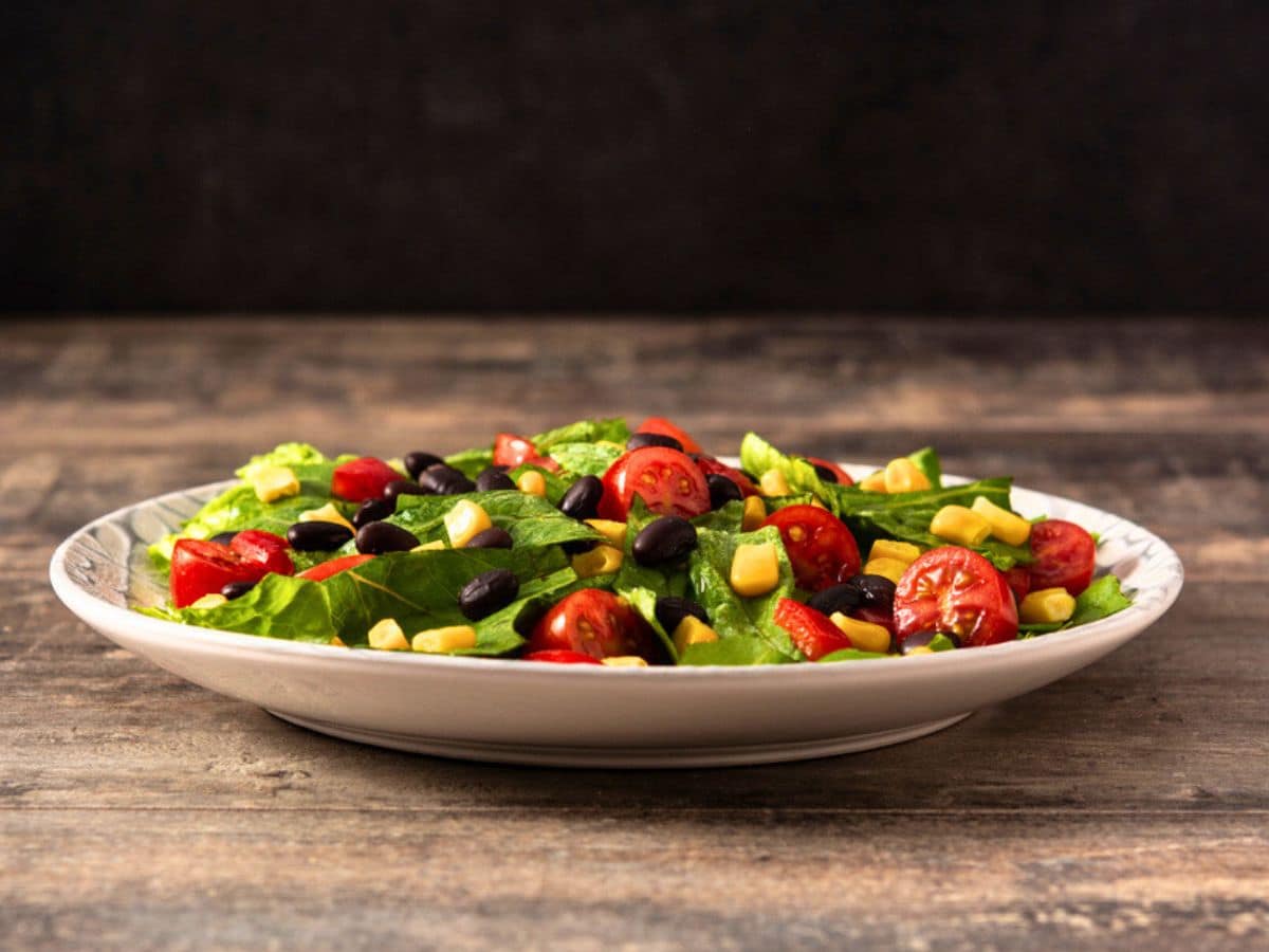 Fresh mixed salad with lettuce, cherry tomatoes, black beans, and corn on a wooden table.