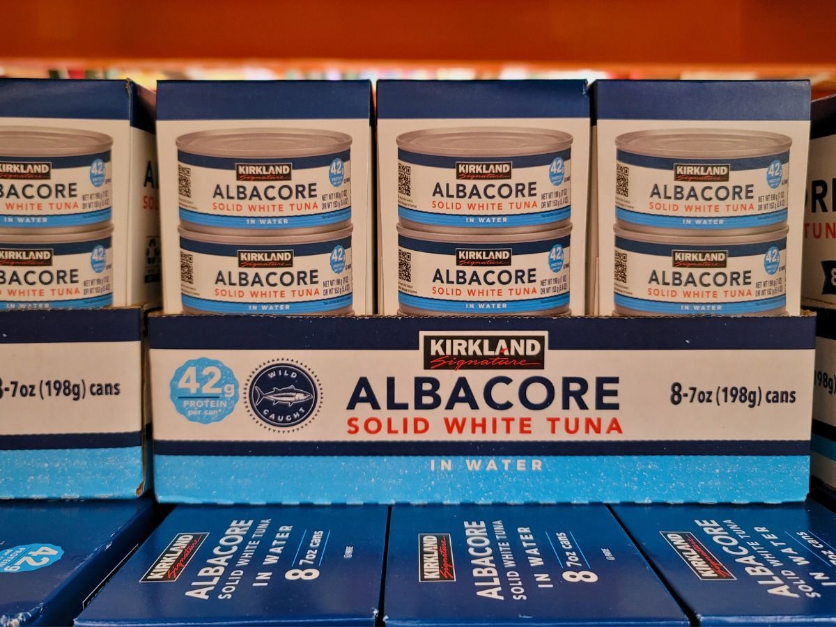 Boxes of Kirkland Signature Albacore Solid White Tuna in water, each containing 8 cans of 198 grams, displayed on a store shelf. The label highlights 42 grams of protein per serving.