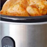 A whole seasoned chicken cooking in a stainless steel slow cooker, with text promoting the best budget-friendly slow cookers for small kitchens.