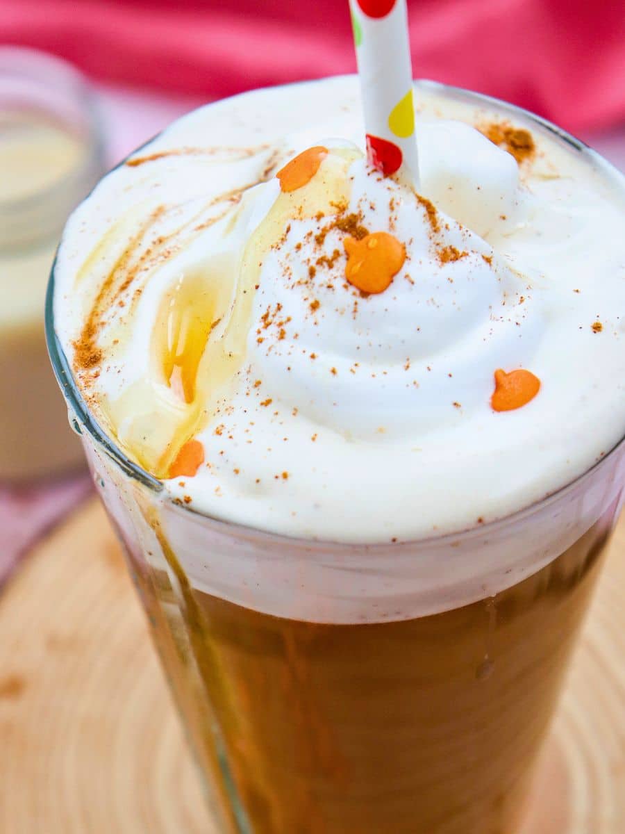 Glass of iced coffee with whipped cream, caramel drizzle, and cinnamon, topped with orange sprinkles, with a colorful straw.