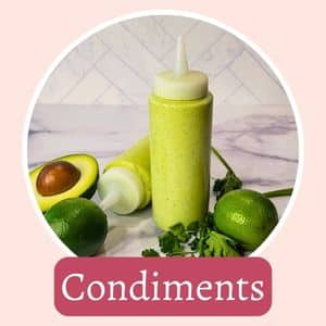 A bottle of green condiment surrounded by halved avocado, lime, and cilantro on a marble surface, labeled "Condiments.