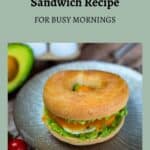 Bagel sandwich with avocado and cheese on a plate, accompanied by an avocado half and eggs in the background. Text reads "Easy Bagel Breakfast Sandwich Recipe for Busy Mornings - Sage AlphaGal.