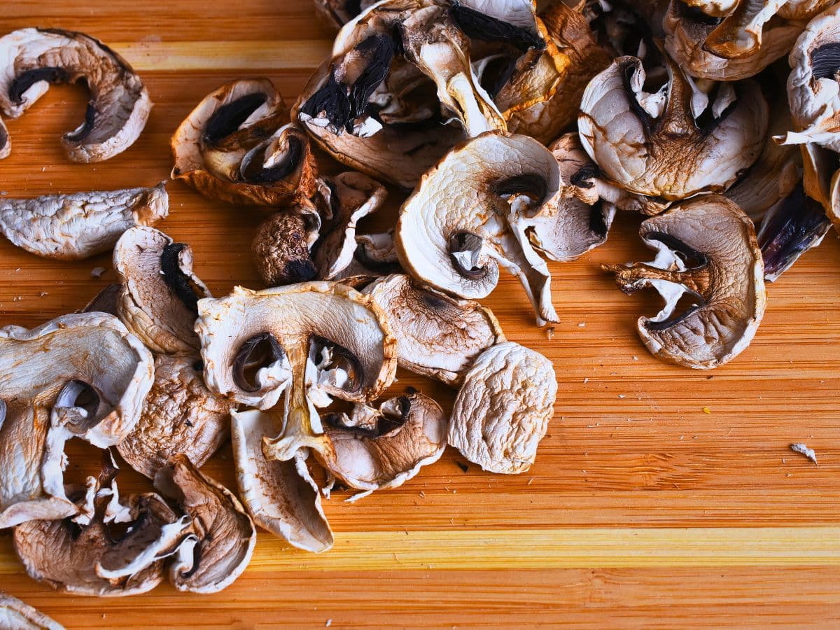 Sliced mushrooms scattered on a wooden cutting board.
