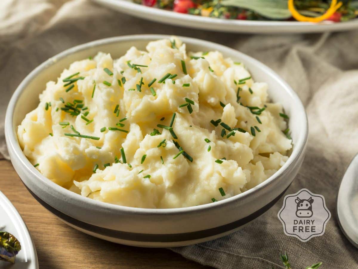 A bowl of dairy-free mashed potatoes topped with chopped chives. A small "dairy-free" label is visible in the corner.