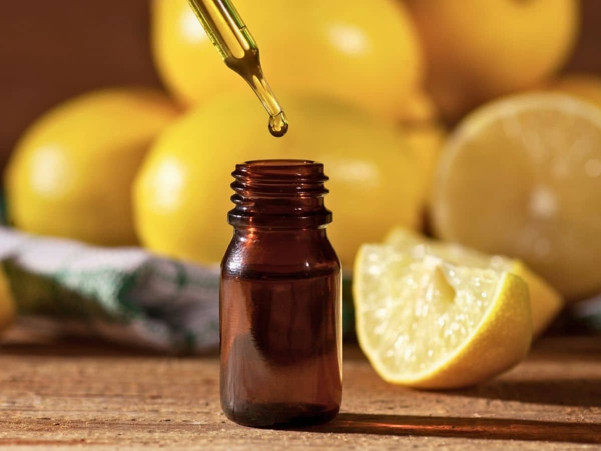 A dropper releases liquid into a small amber glass bottle, with whole and sliced lemons in the background on a wooden surface.